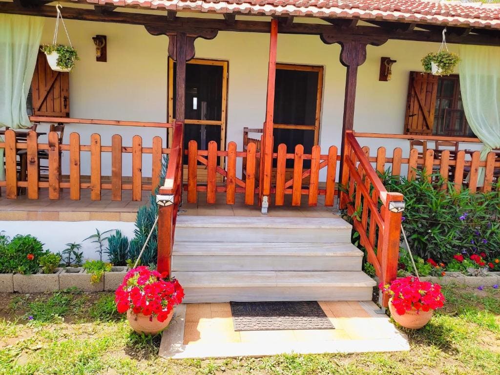 RODAVGI front entrance with wooden veranda, flower pots, and lush garden